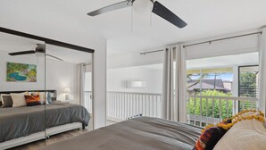 Un dormitorio moderno con una cama grande, un ventilador de techo y un balcón con barandilla blanca.