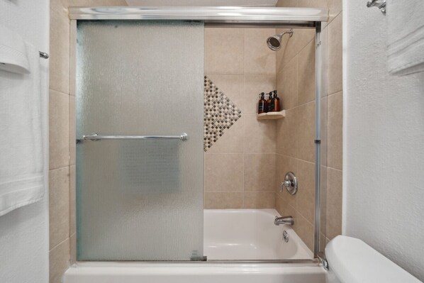 A shower enclosure with a glass door, a showerhead, and a shelf with toiletries.