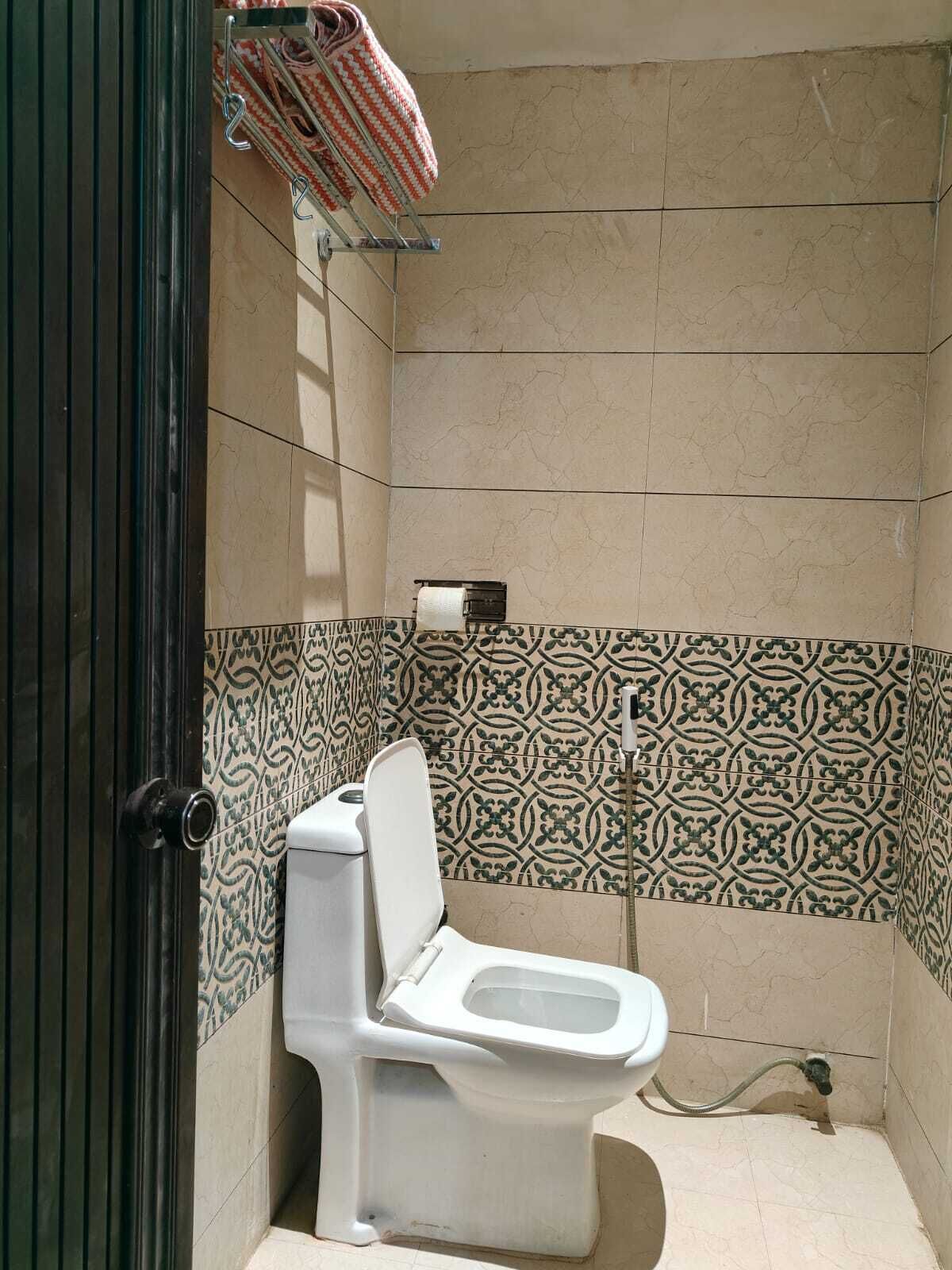 Un baño pequeño con azulejos, un inodoro, un perchero y un papel tapiz estampado.