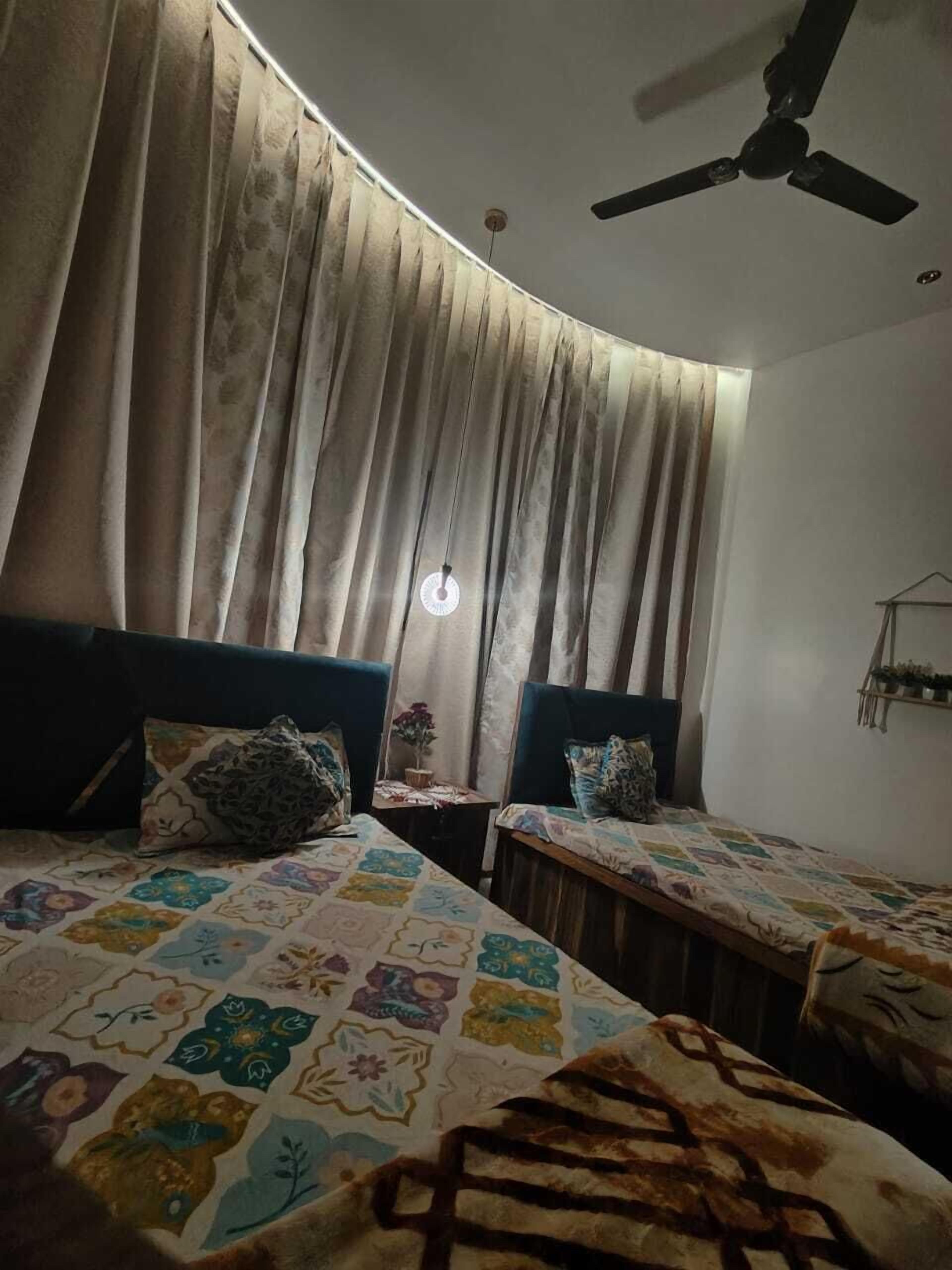 A room with two beds, a ceiling fan, and a small table with a plant.