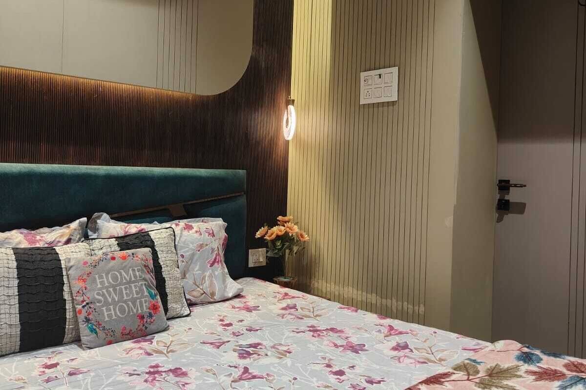 A bedroom with a bed, pillows, a bedside table with a vase of flowers, and a wall-mounted air conditioner.