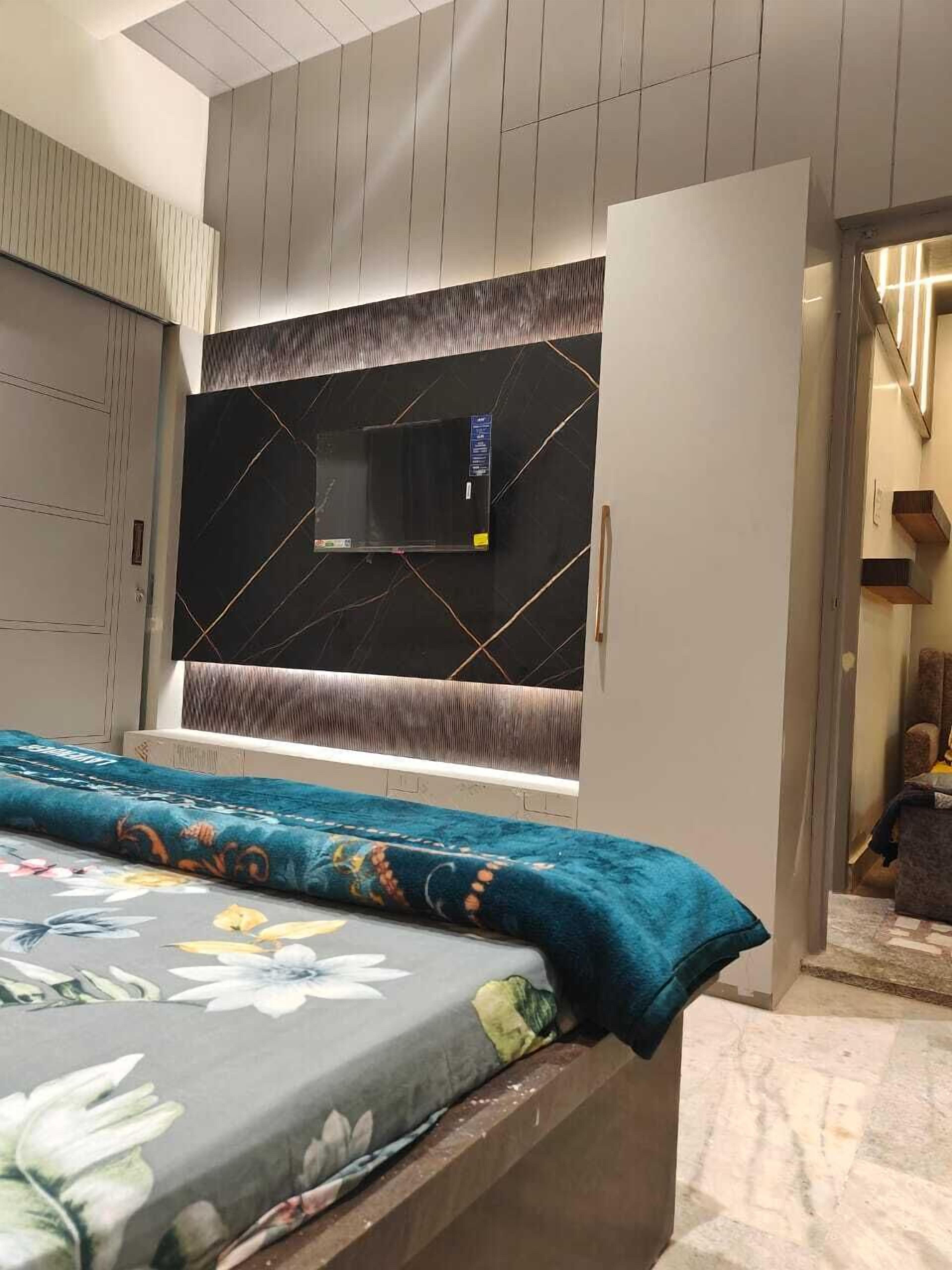 A modern bedroom with a bed, a TV mounted on a black marble wall, and a wardrobe.