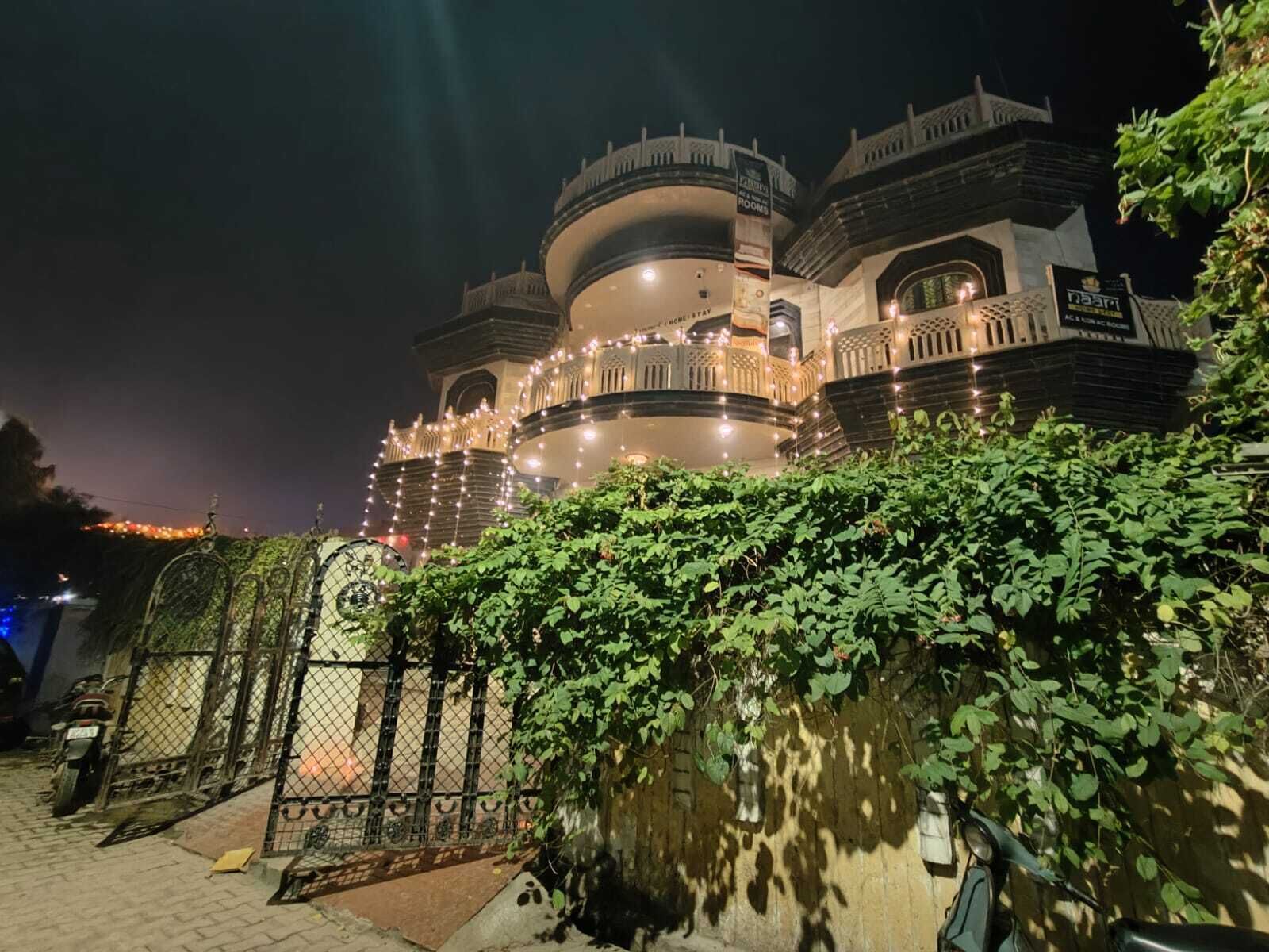 A large, multi-story building with a dome and multiple balconies, surrounded by greenery and a gated entrance.