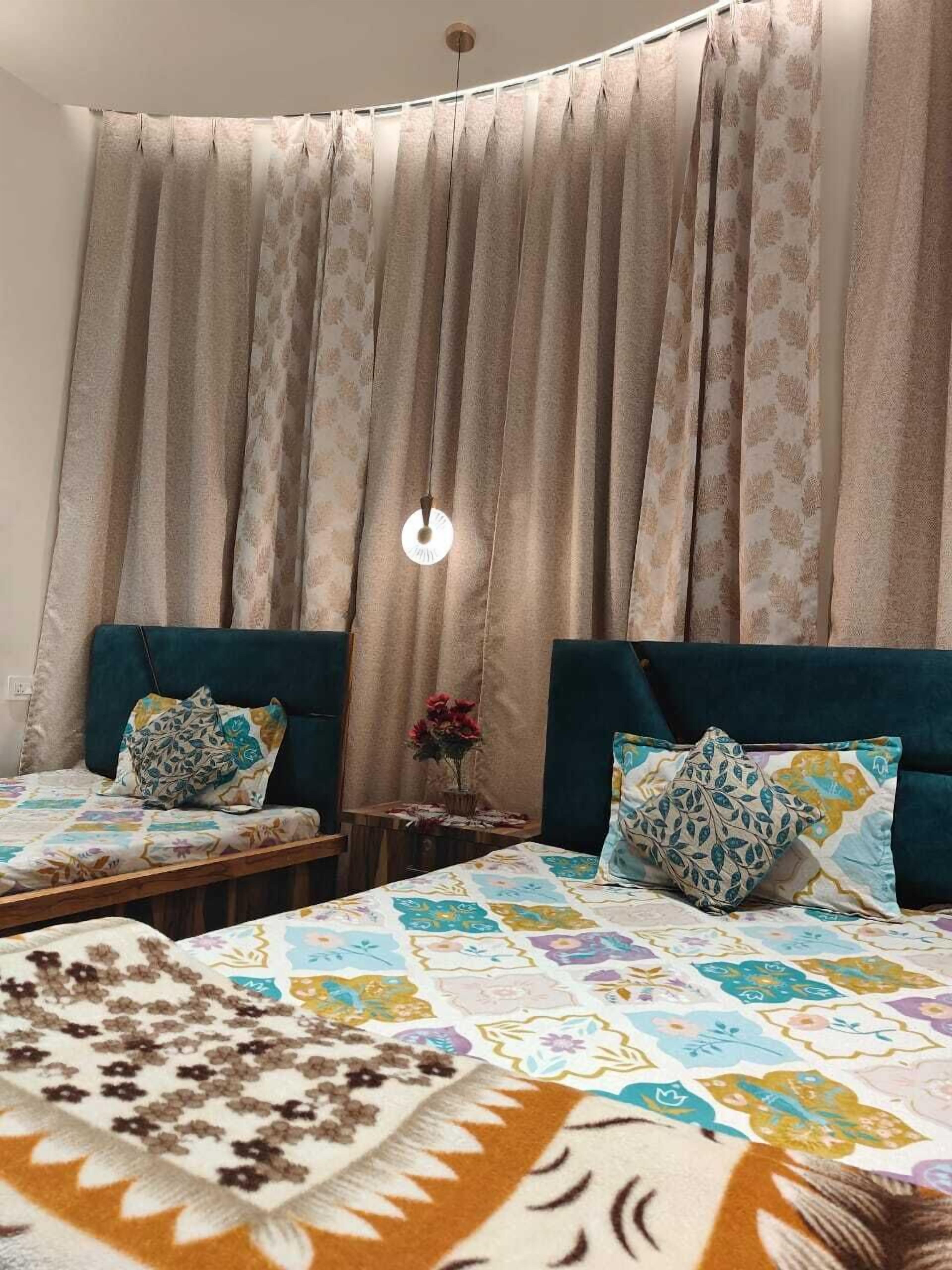 A bedroom with two beds, a hanging light fixture, and a small table with a vase of flowers.