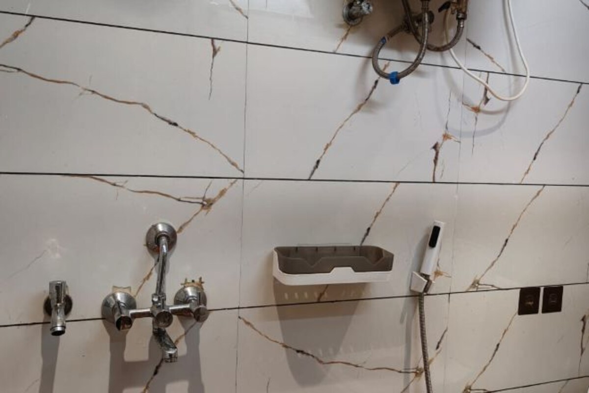 Un baño con zócalos de mármol blanco, ducha con cabezal de ducha manual, dispensador de jabón y perchero.