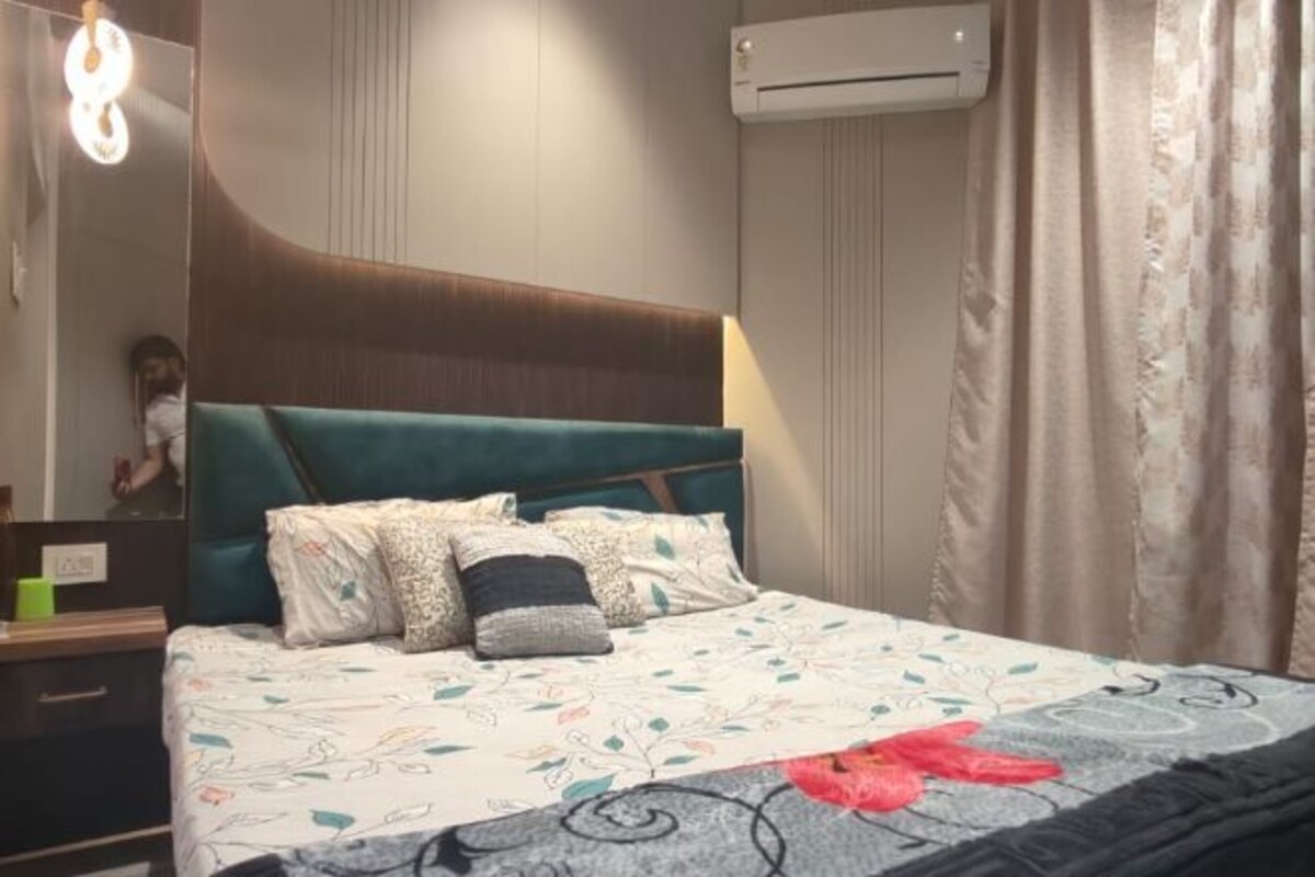 A bedroom with a bed, a headboard, a bedside table, a mirror, and an air conditioning unit.