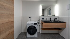 Ein kleines, modernes Badezimmer mit integrierter Waschmaschine und Trockner, einem Holz-Waschtisch und einem Spiegel über dem Waschbecken.