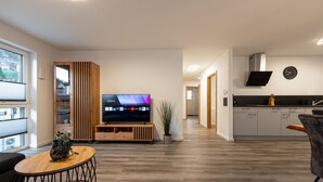 Ein modernes Wohnzimmer mit Flachbildfernseher, Holzboden und einem Essbereich mit Tisch und Stühlen.