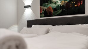 Ein Schlafzimmer mit Bett, weißer Bettwäsche, einer Wandleuchte und einem Landschaftsbild.
