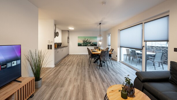 Ein modernes Wohnzimmer mit Fernseher, Essbereich und großen Fenstern.