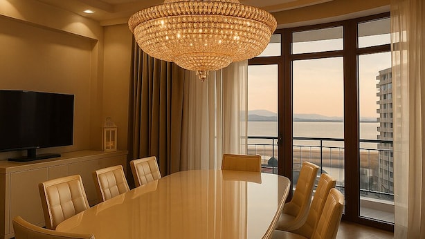 A spacious dining area with a large round table and comfortable chairs, a modern chandelier, a flat-screen TV, and a view of a body of water through large windows. - Baku Lake view 3 bedrooms apartment (Baku)