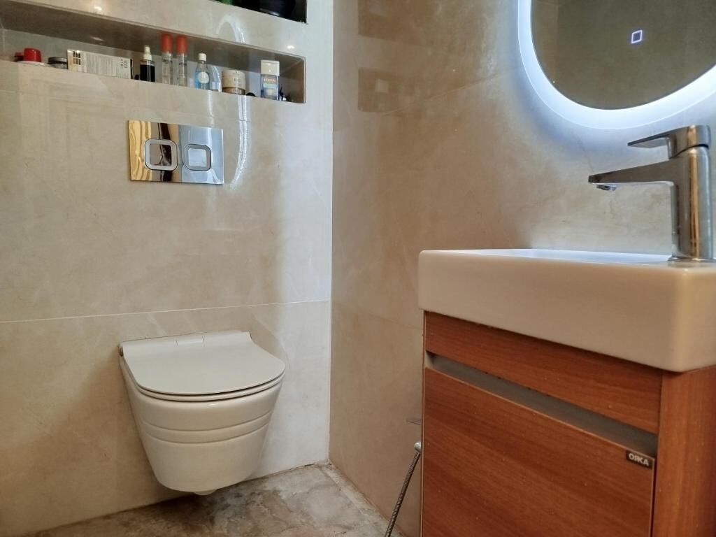 Un baño con un inodoro, un armario de madera y un estante con artículos de aseo.