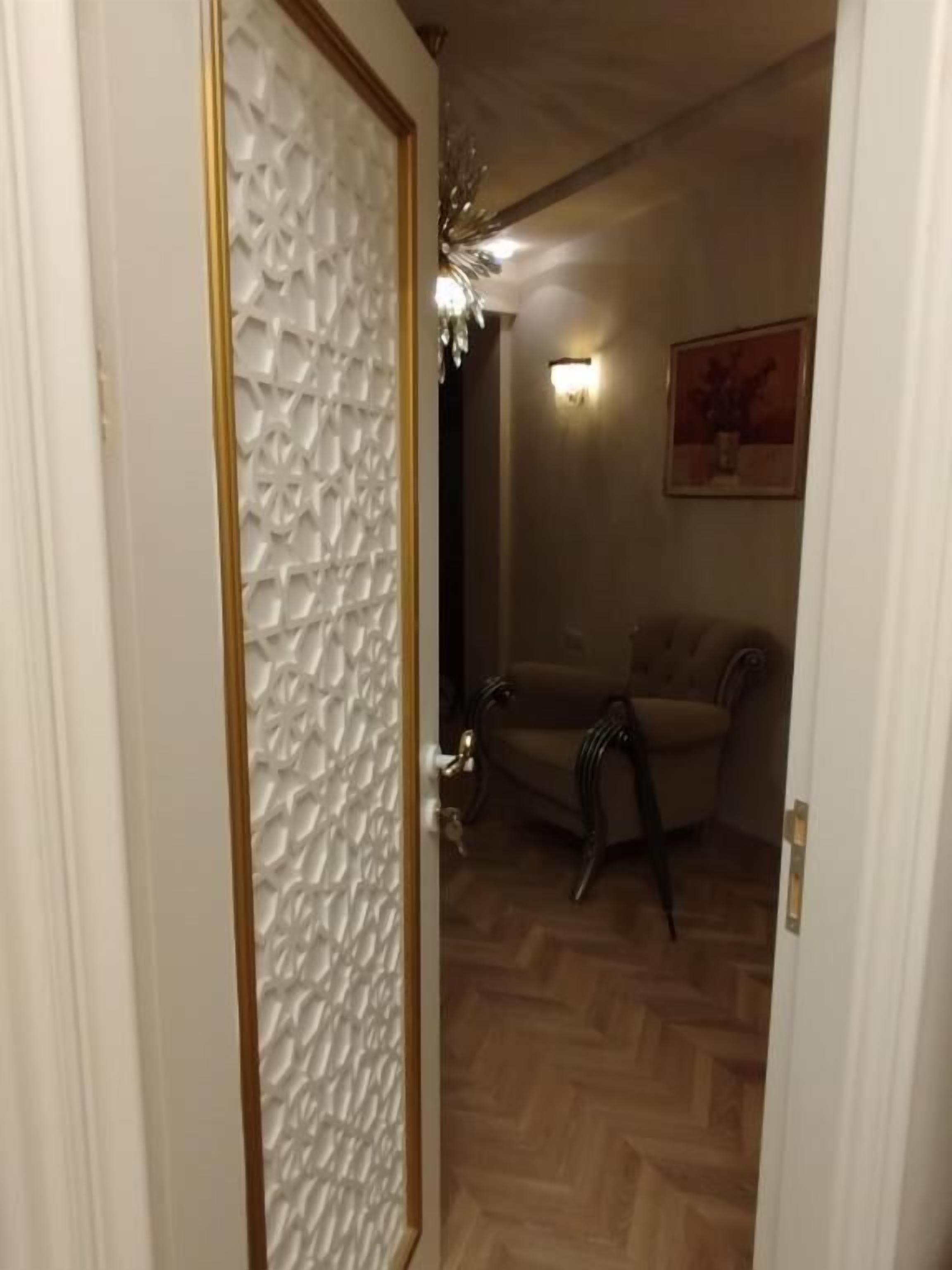 A room with a patterned door, a sofa, a lamp, and a painting on the wall.