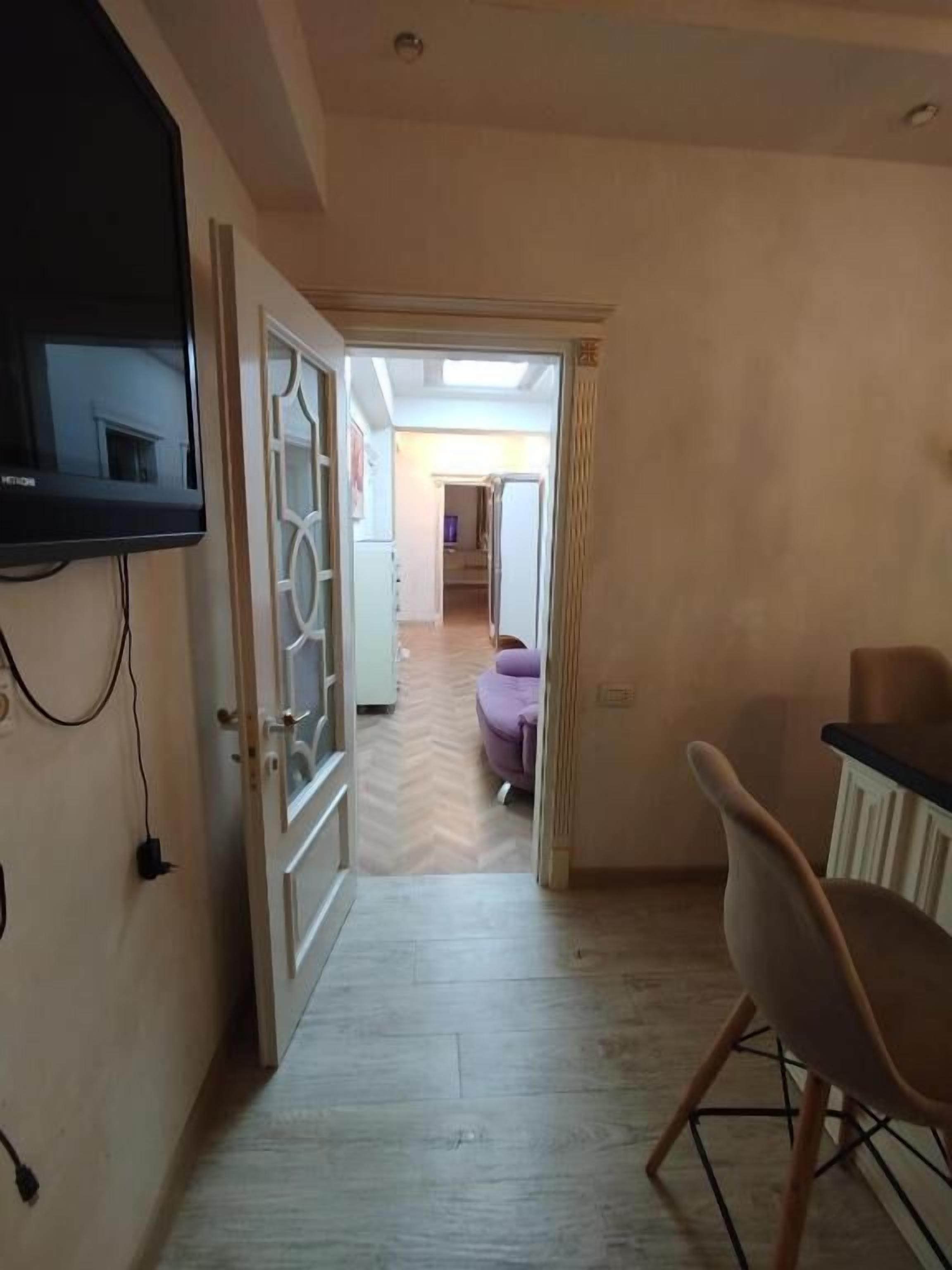 Une pièce avec un téléviseur fixé au mur, une porte donnant sur une autre pièce, une chaise et une table.