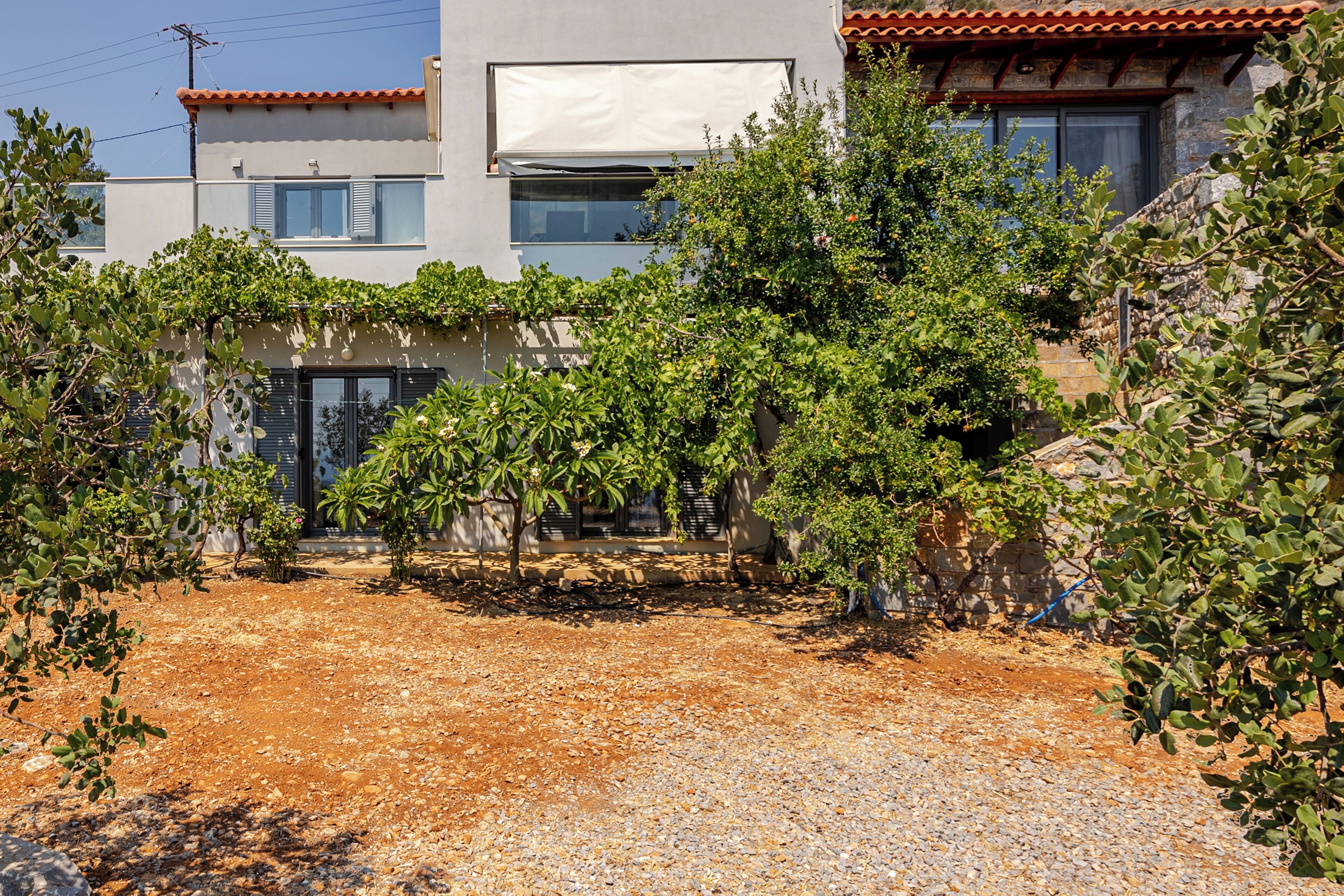 A modern building with a gravel courtyard, surrounded by lush greenery and stone walls.