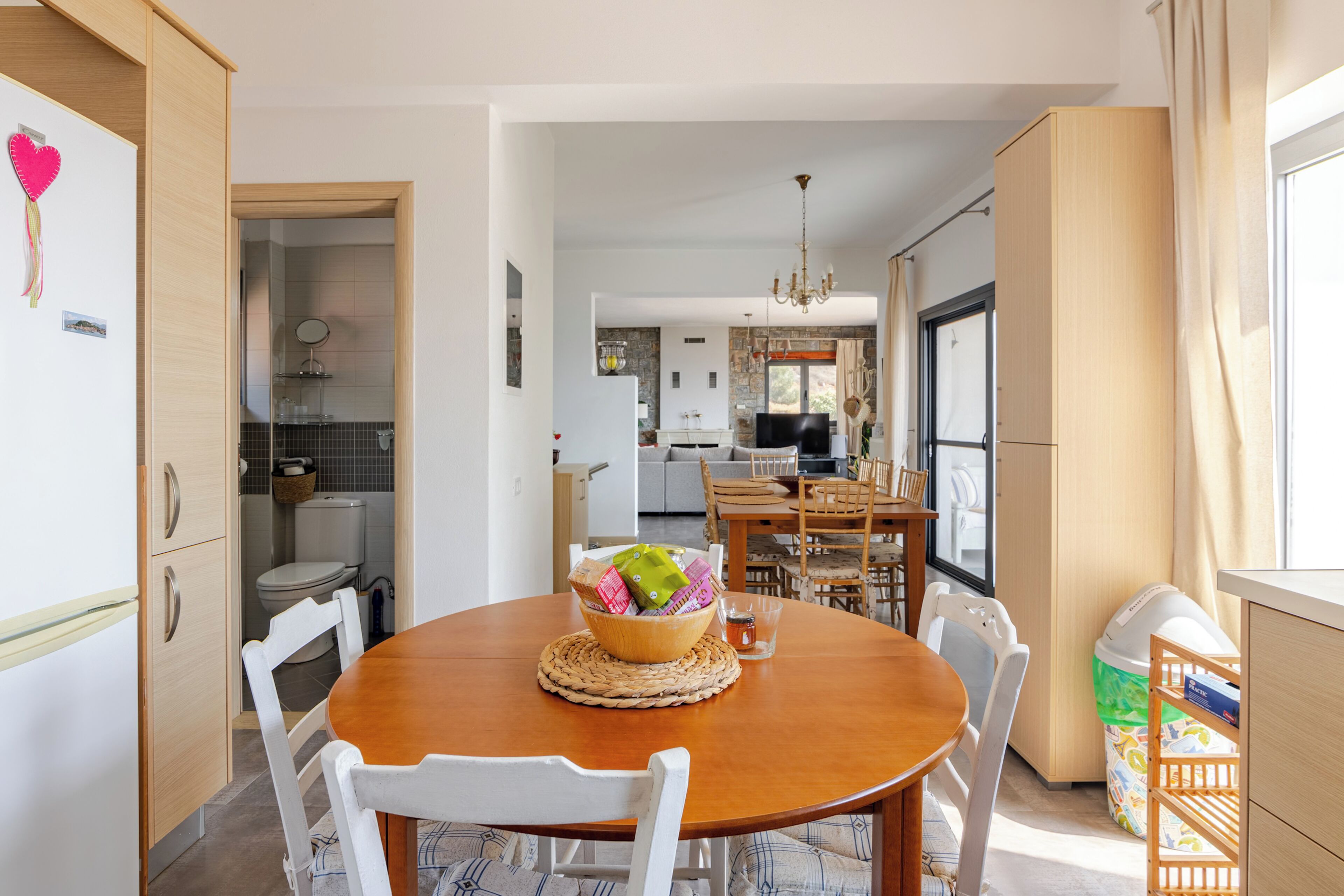 A modern kitchen with a dining area, wooden cabinets, and a chandelier.