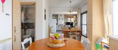 A modern kitchen with a dining area, wooden cabinets, and a chandelier.