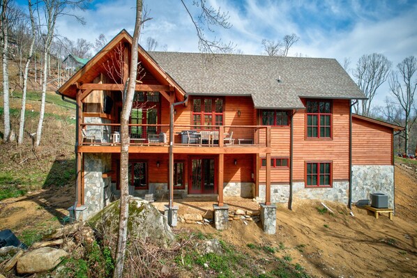 A large, two-story wooden cabin with a stone foundation, multiple windows, and a balcony.
