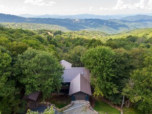 A house surrounded by dense forest with a view of distant mountains.