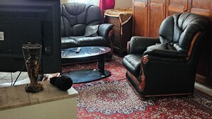 A living room with a television, leather chairs, a red patterned carpet, and a wooden wardrobe.