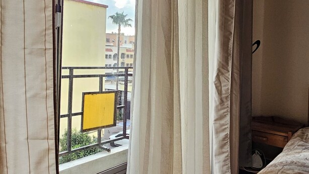 A room with a bed, curtains, and a view of the outside balcony.