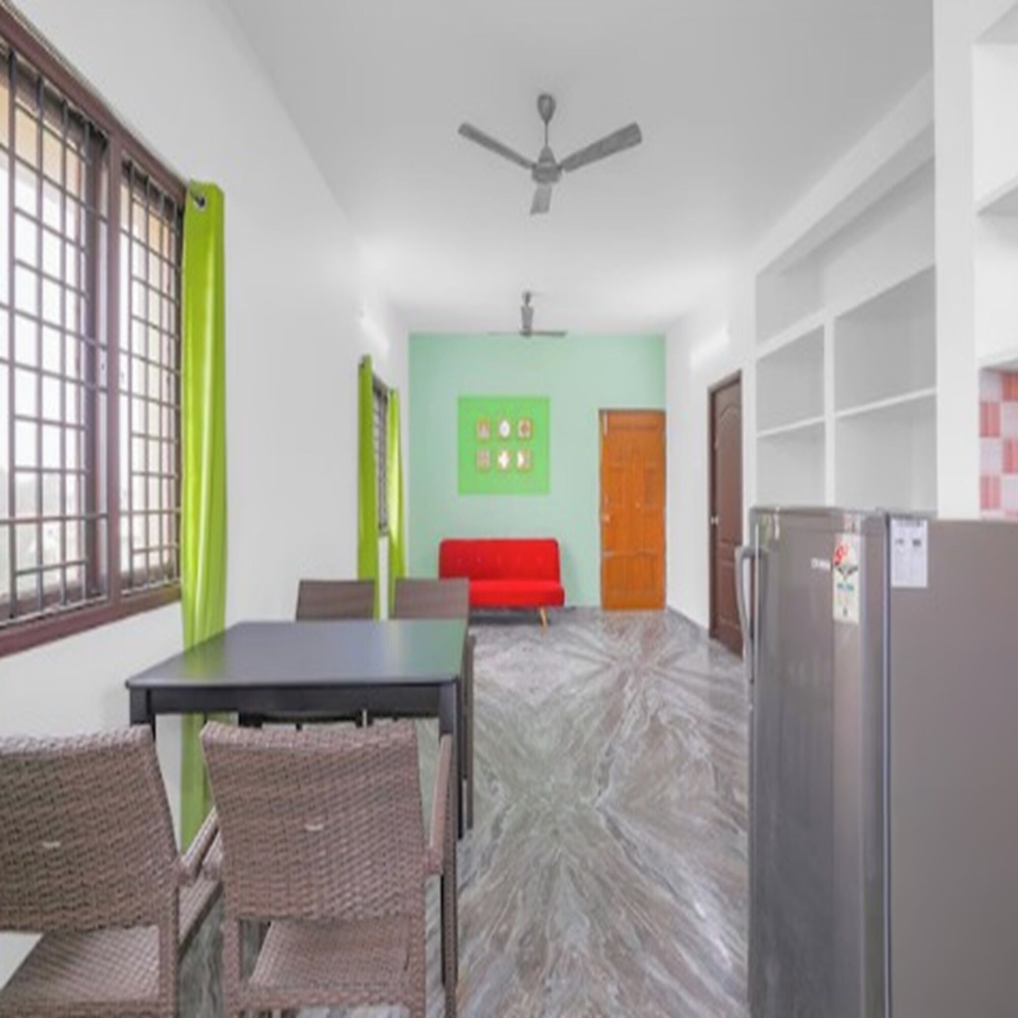 A room with a table and chairs, a refrigerator, a ceiling fan, and a door.