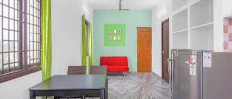 A room with a table and chairs, a refrigerator, a ceiling fan, and a door.