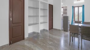 Une pièce spacieuse avec une porte en bois, des étagères intégrées, un coin repas avec des chaises et un ventilateur de plafond.