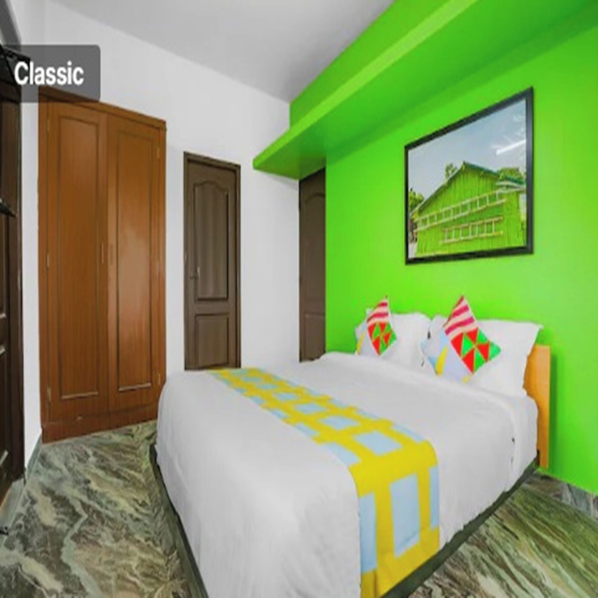 A room with a bed, a wooden wardrobe, and a green wall with a framed picture.