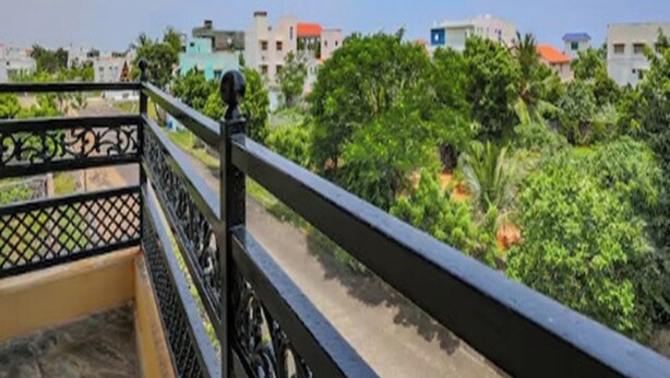 Un balcon doté d’une rambarde en métal, donnant sur un quartier résidentiel avec des maisons et de la verdure.