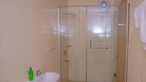 Casa de banho com chuveiro envidraçado, pia branca e um frasco verde de sabonete.