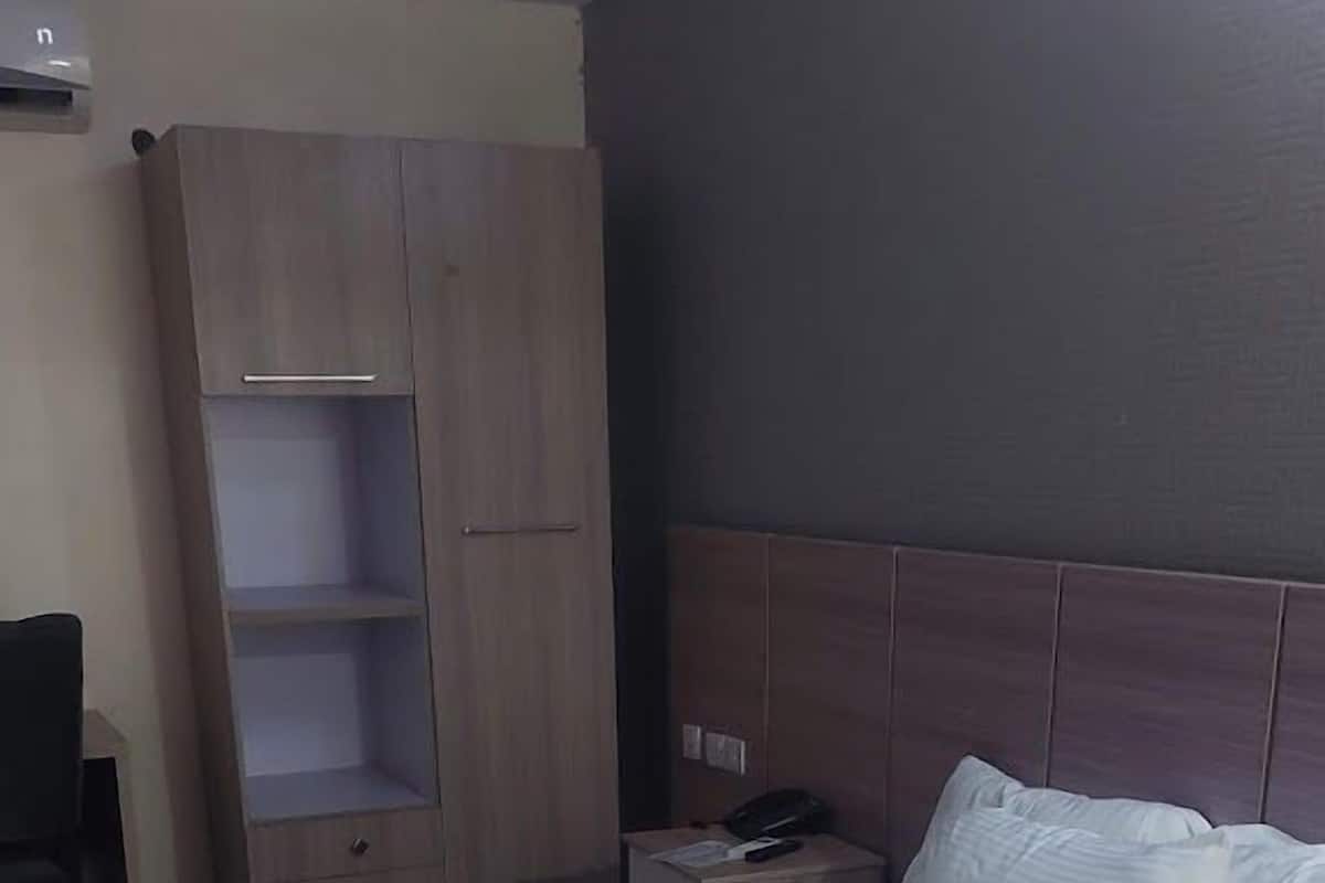 A hotel room with a large bed, a wooden wardrobe, a nightstand, and a desk.