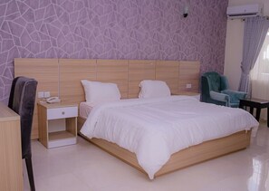 Un dormitorio moderno con una cama grande, cabecera de madera, una mesita de noche con un teléfono, una silla y una pequeña mesa.
