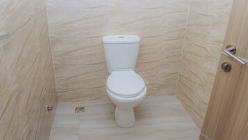 Une salle de bain moderne avec des toilettes blanches, des murs carrelés et une porte en bois.