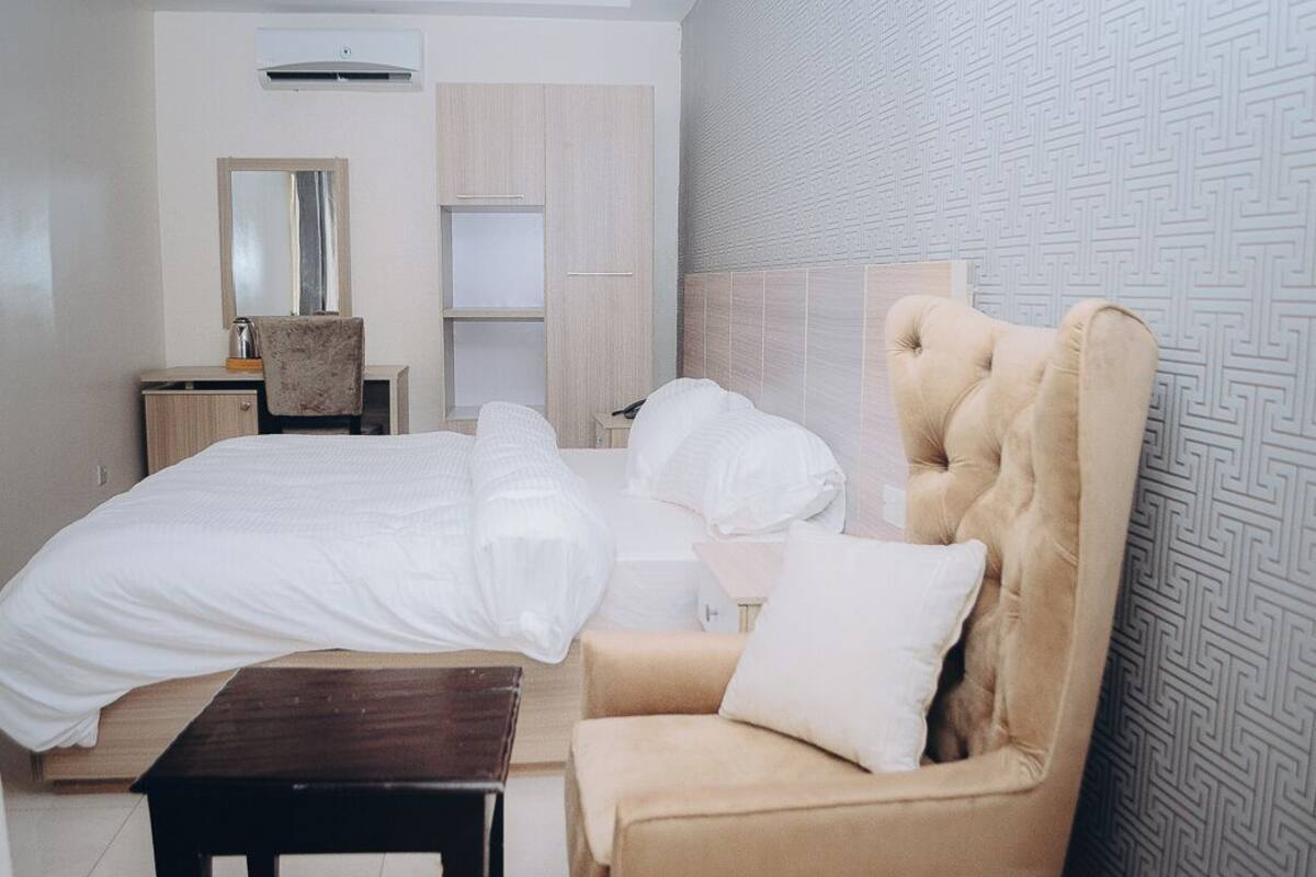 A hotel room with a large bed, a chair, a desk, and a mirror.