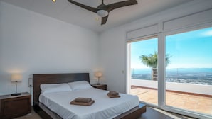 Una camera da letto con un letto grande, due comodini, un ventilatore a soffitto e vista sulla città attraverso una porta scorrevole in vetro.