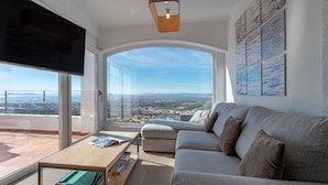 Un soggiorno moderno con un divano grigio, un tavolino in legno e un'ampia finestra con vista sulla città.