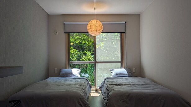Un dormitorio con dos camas, un ventanal grande y una lámpara colgante.