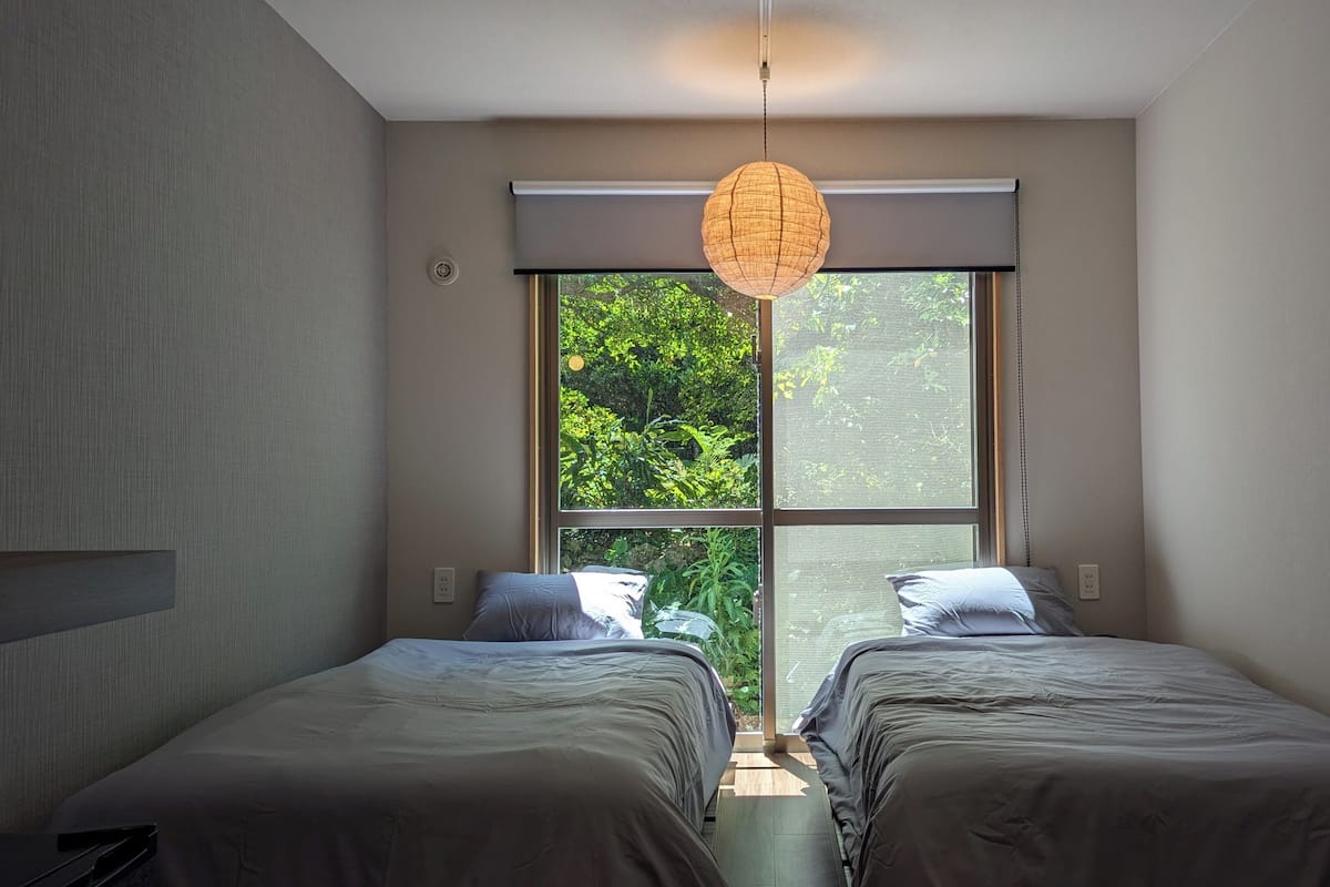 Ein Schlafzimmer mit zwei Betten, einem großen Fenster und einer Pendelleuchte.