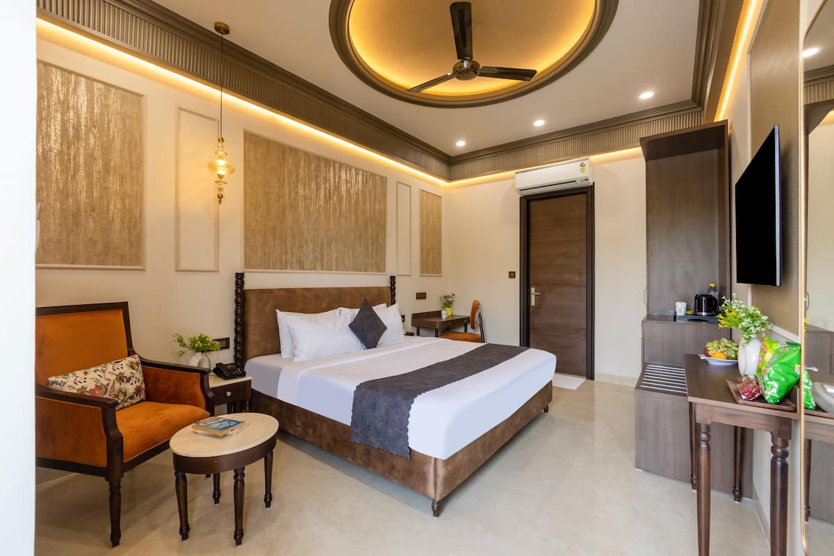 Habitación de hotel con una cama grande, una silla, una mesita pequeña, un ventilador de techo y un televisor en la pared.