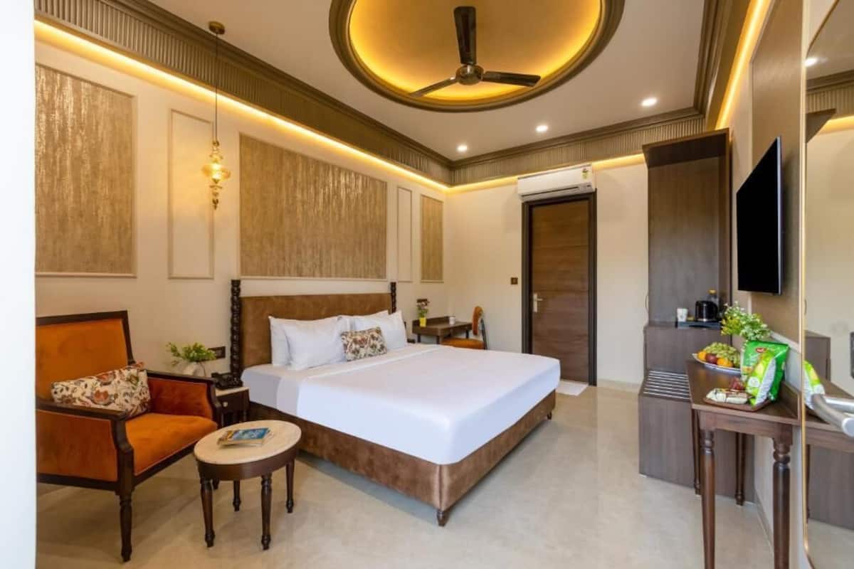 Habitación de hotel con una cama grande, un escritorio, una silla, una mesita, un ventilador de techo y un televisor.