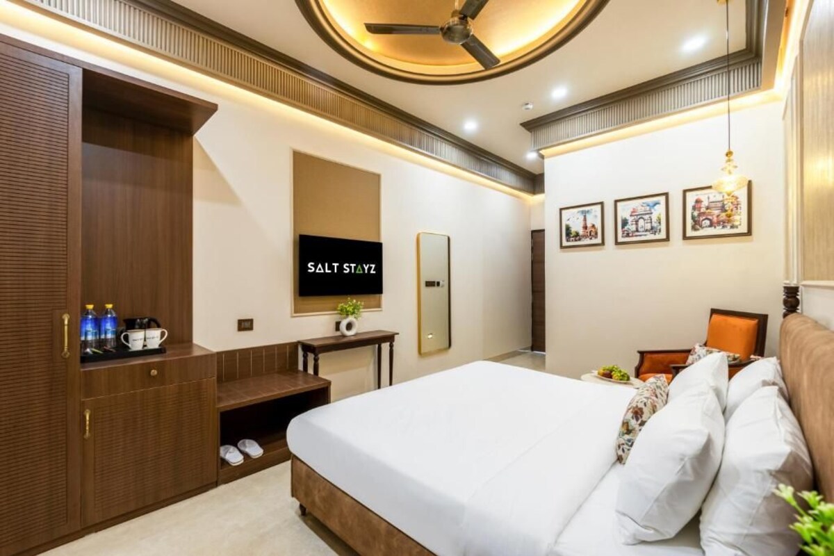 A hotel room with a bed, a TV, a wardrobe, and a small table with a plant.