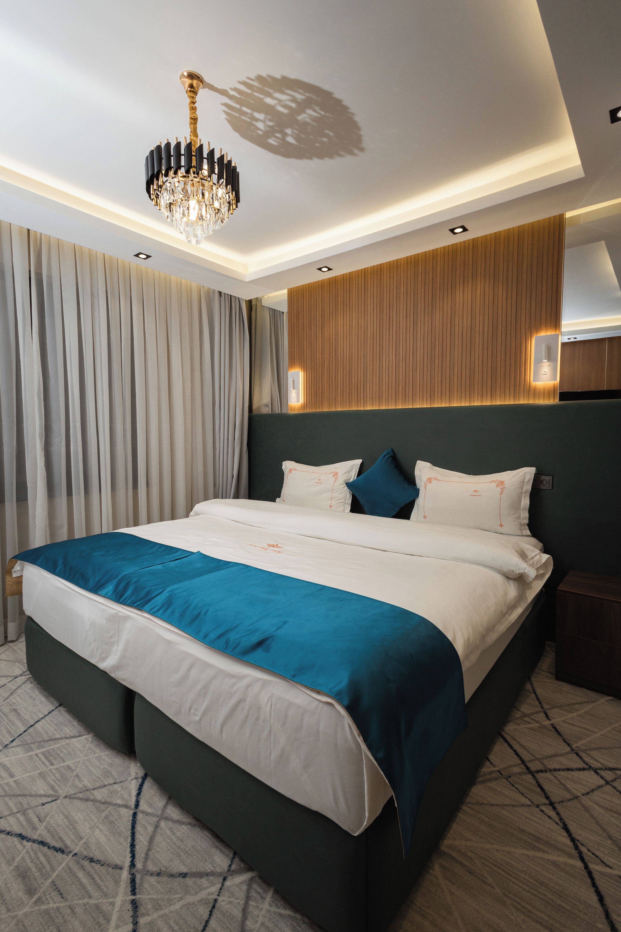 A modern hotel room with a large bed, a chandelier, and a wooden accent wall.