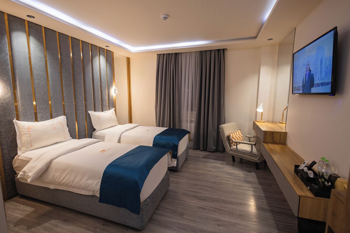 A hotel room with two beds, a desk, a chair, a TV, and a window with curtains.