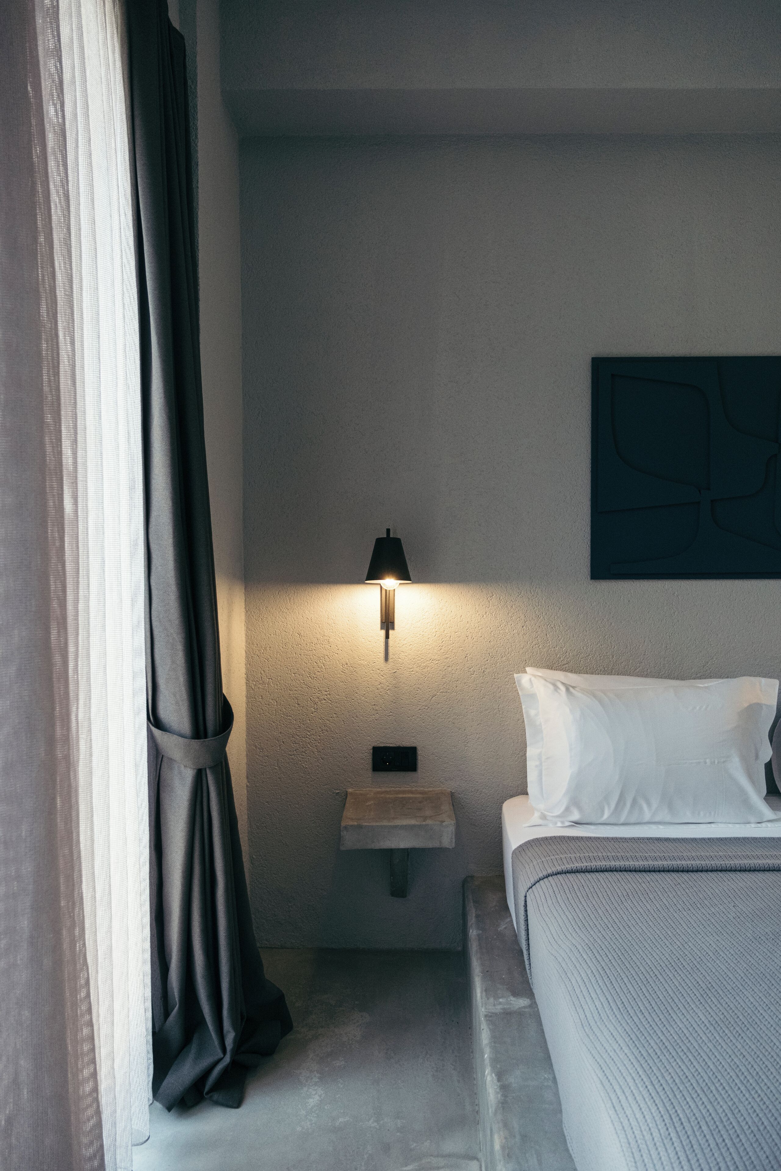 Ein Hotelzimmer mit Bett, Nachttisch, Wandlampe und einem Gemälde.