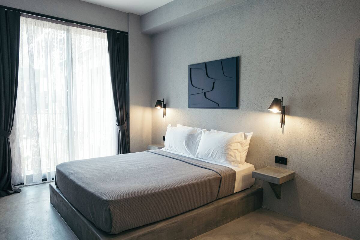 A modern bedroom with a large bed, a bedside table, a wall-mounted artwork, and a window with curtains.