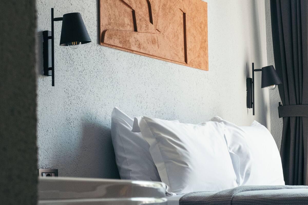 A modern hotel room with a bed, a wall-mounted artwork, and a window with curtains.