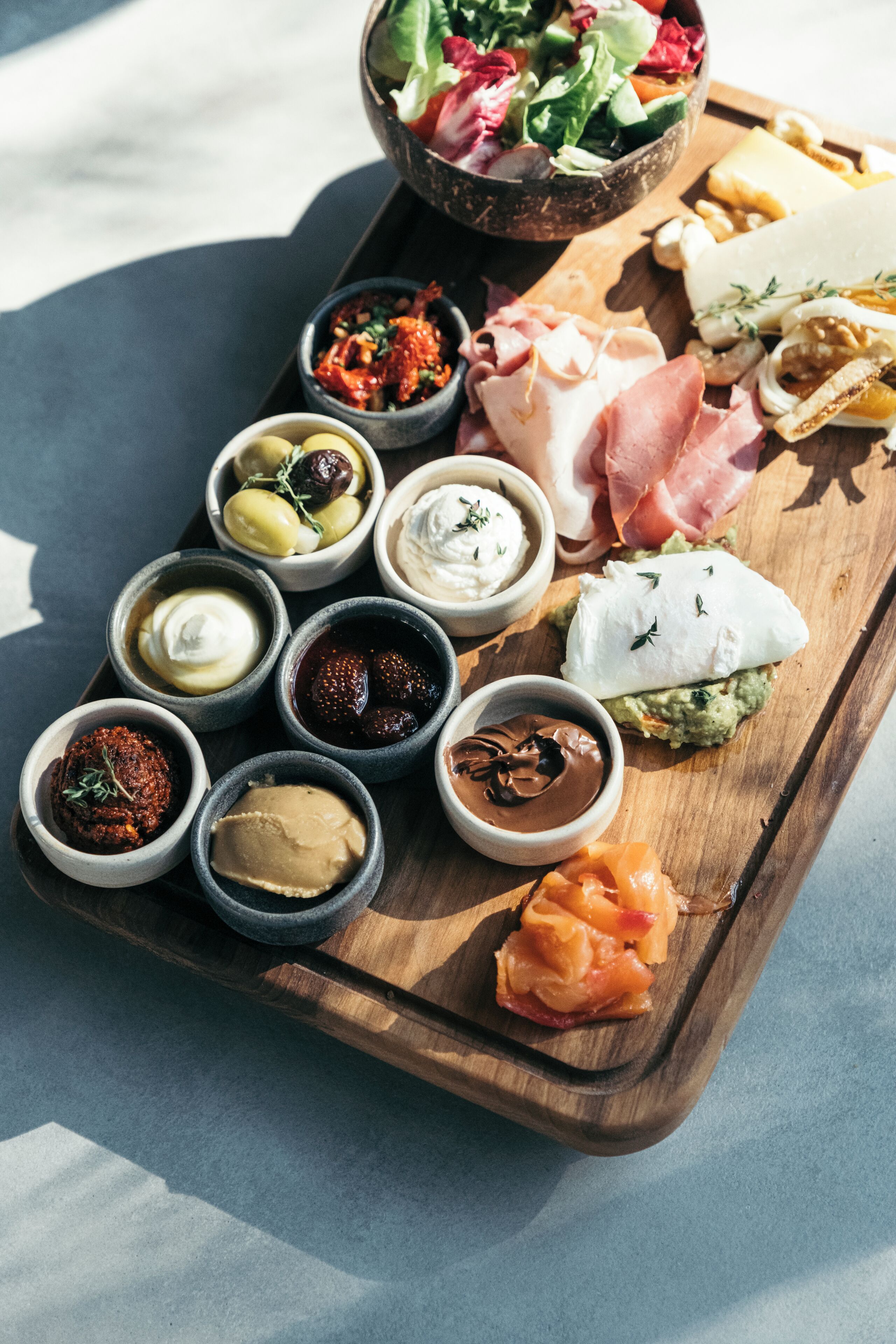 Une planche en bois sur laquelle sont disposés divers aliments, notamment du fromage, de la charcuterie et des sauces.