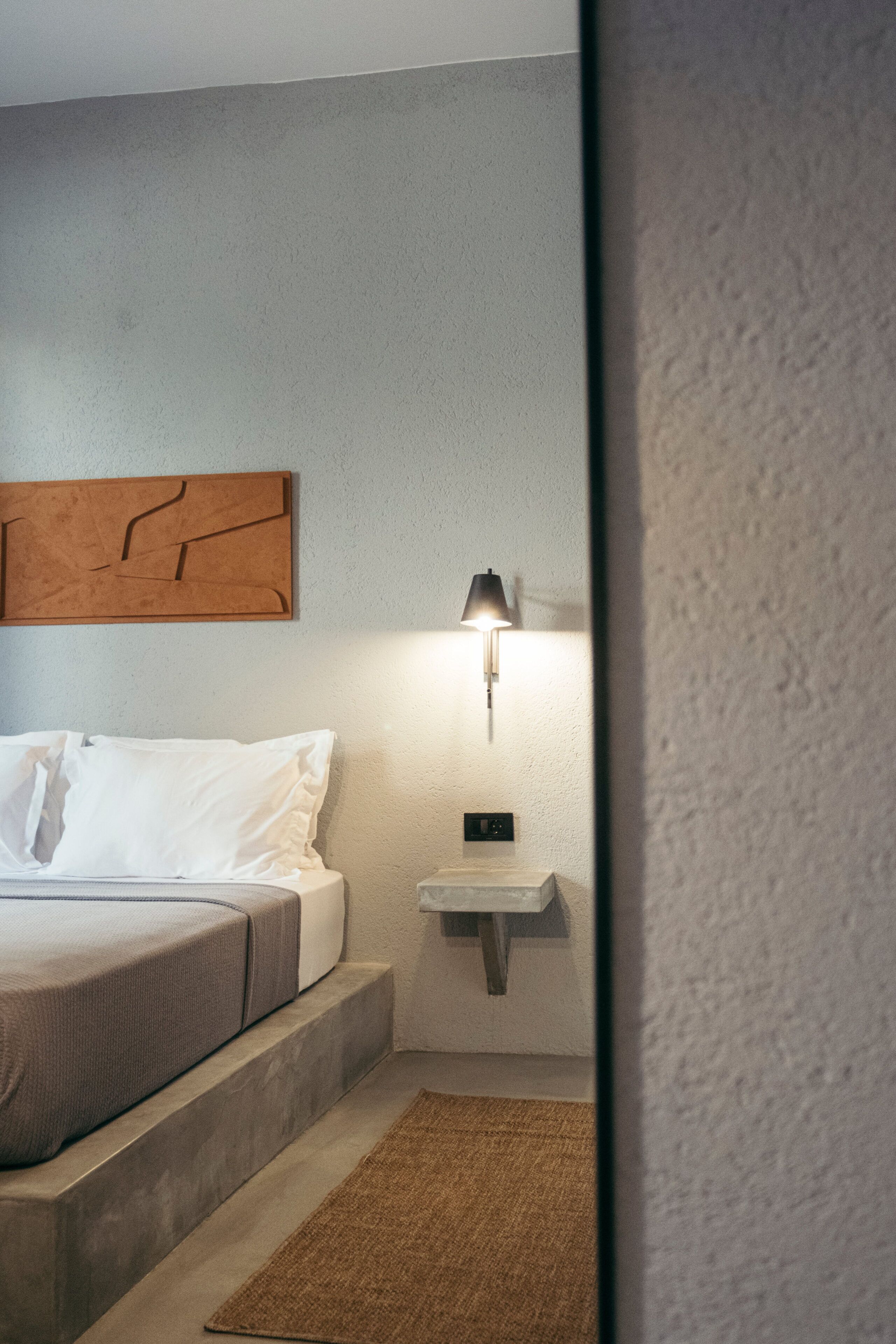 A bedroom with a bed, a nightstand, a wall-mounted lamp, and a piece of wall art.