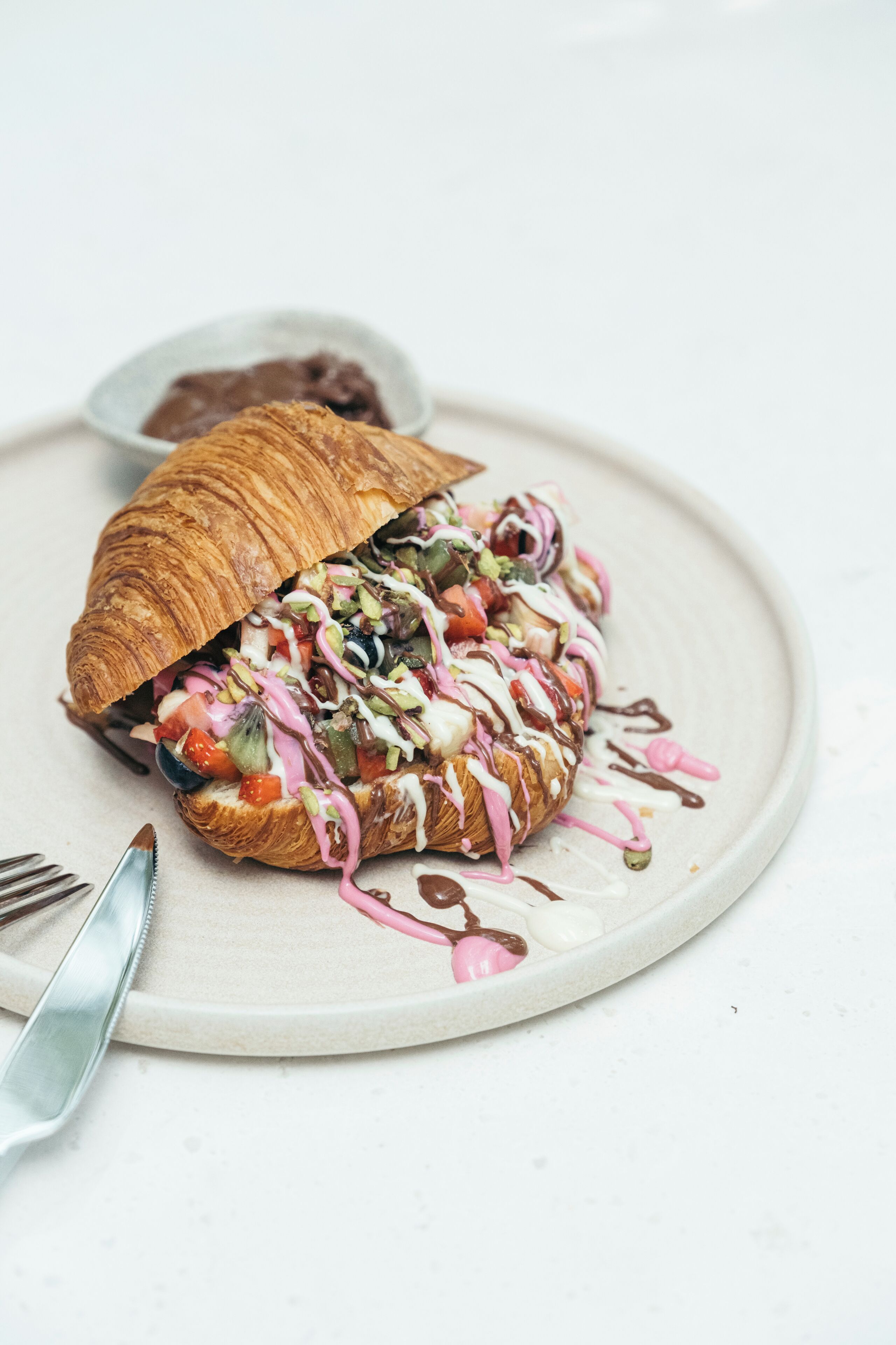 Een croissant belegd met diverse ingrediënten en sauzen op een bord.